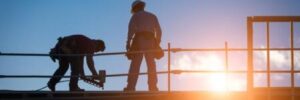 Two men work on a commercial roof as the sun sets