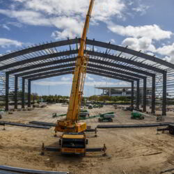 Three cranes loading beams onto a steel structure.